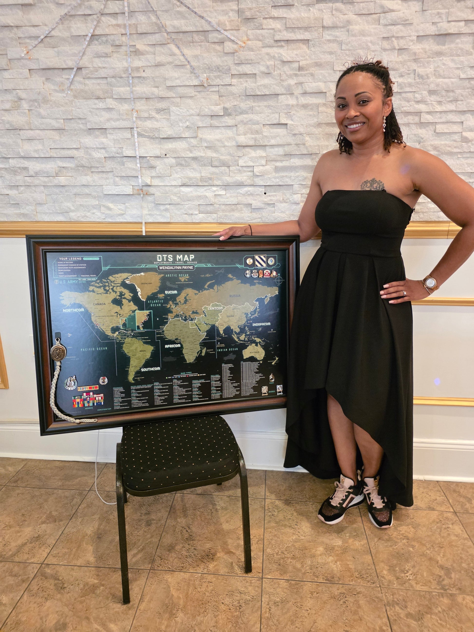 Woman in a black dress standing next to a framed world map on a chair.