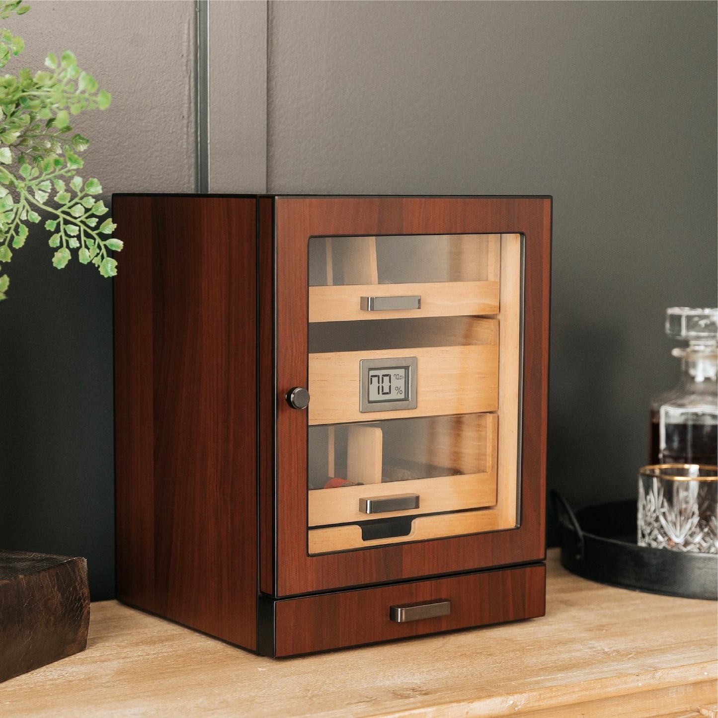 Wooden humidor with glass door on a wooden surface against a gray wall.