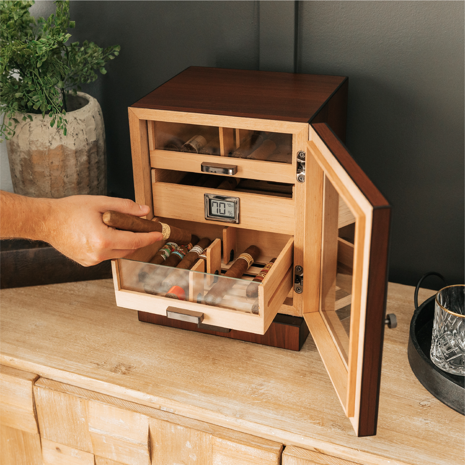 Wooden humidor with a hand reaching in to take out a cigar, placed on a wooden surface.