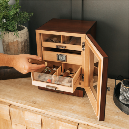 Wooden humidor with a hand reaching in to take out a cigar, placed on a wooden surface.