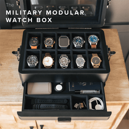 Military modular watch box with multiple watches displayed on a wooden surface
