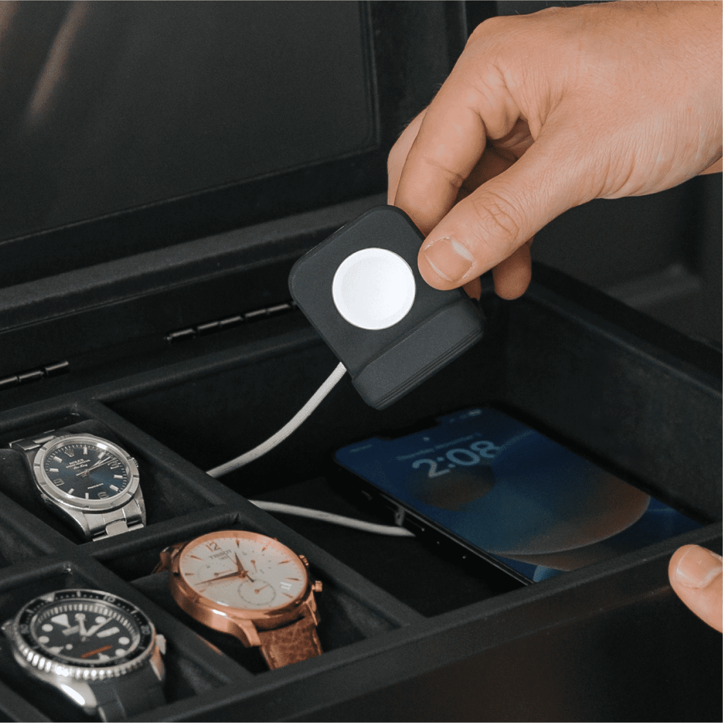 Hand holding a small device over a collection of watches in a display case.