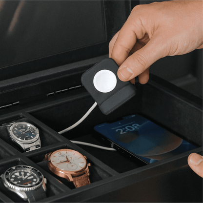 Hand holding a small device over a collection of watches in a display case.