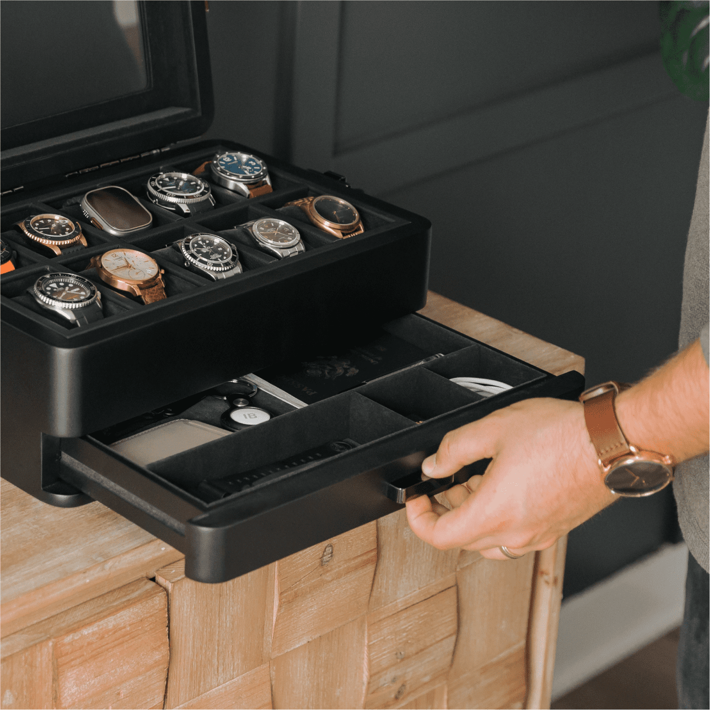 Black watch storage case with multiple watch compartments on a wooden surface.