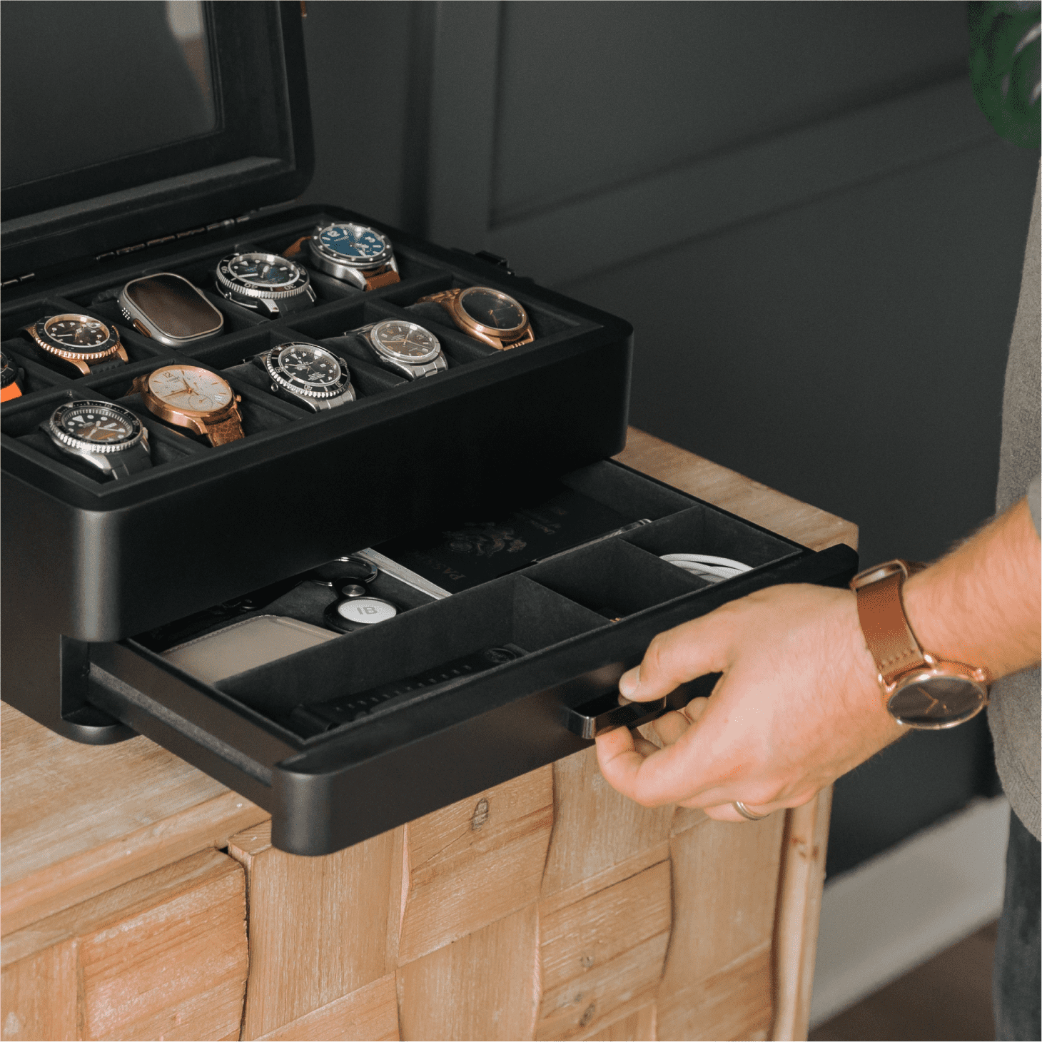 Black watch storage case with multiple watch compartments on a wooden surface.
