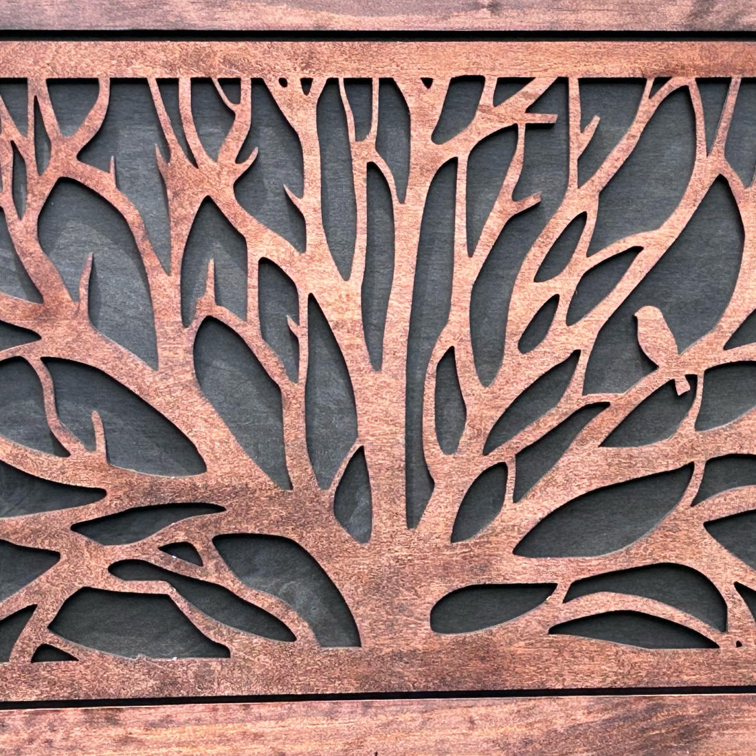 Decorative metal panel with tree branch and leaf pattern on a wooden background