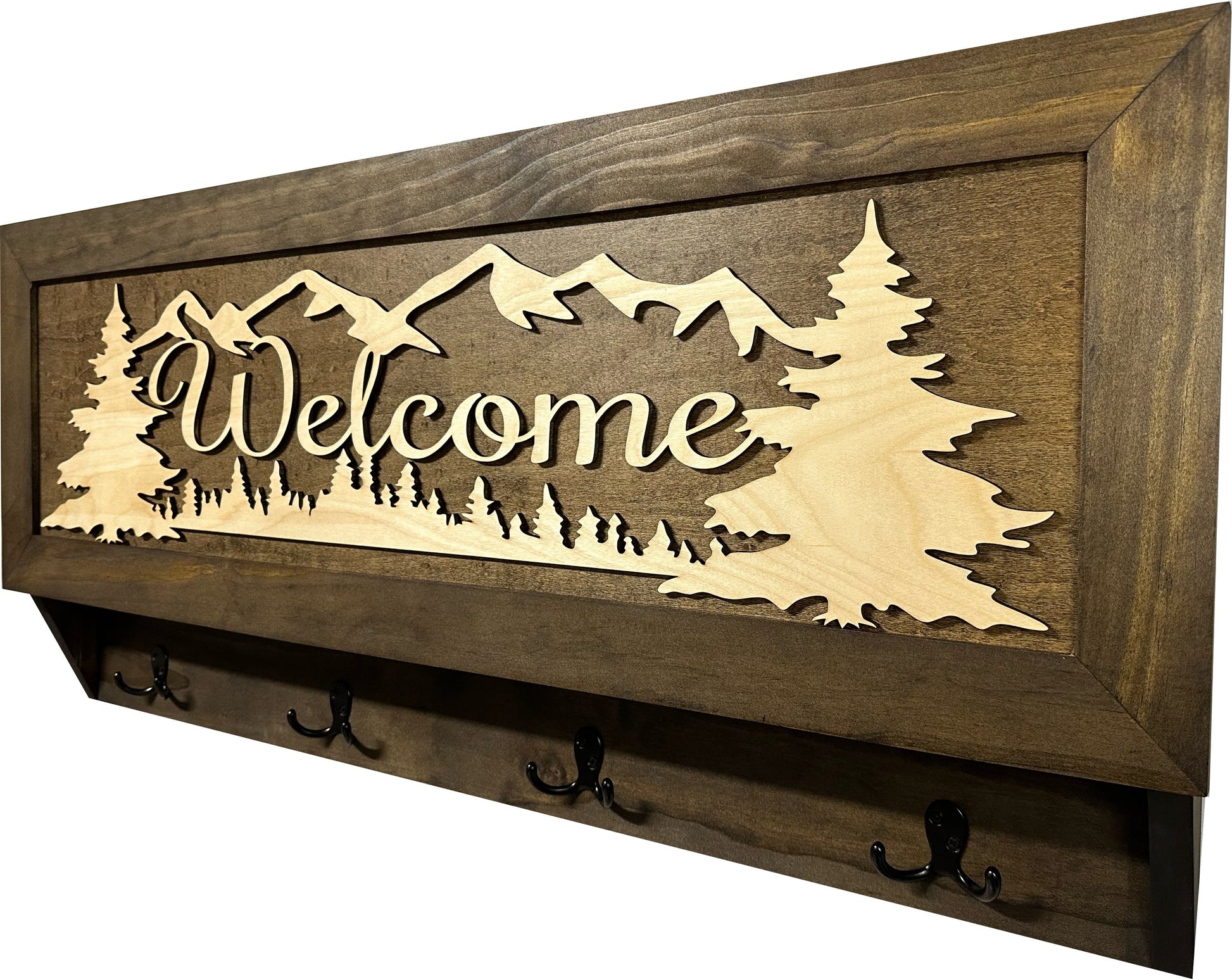 Wooden wall decor with 'Welcome' and mountain design, featuring hooks on a white background.