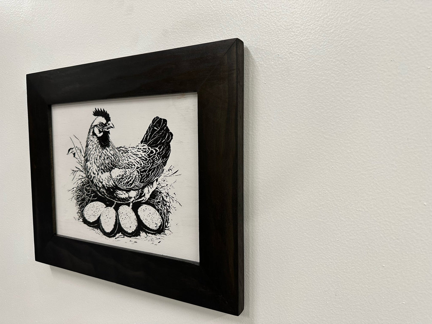 Framed black and white illustration of a rooster on a light gray wall.