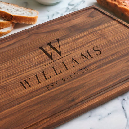 Wooden cutting board with engraved 'WILLIAMS' and 'EST 9-19-20' on a marble surface with bread slices.